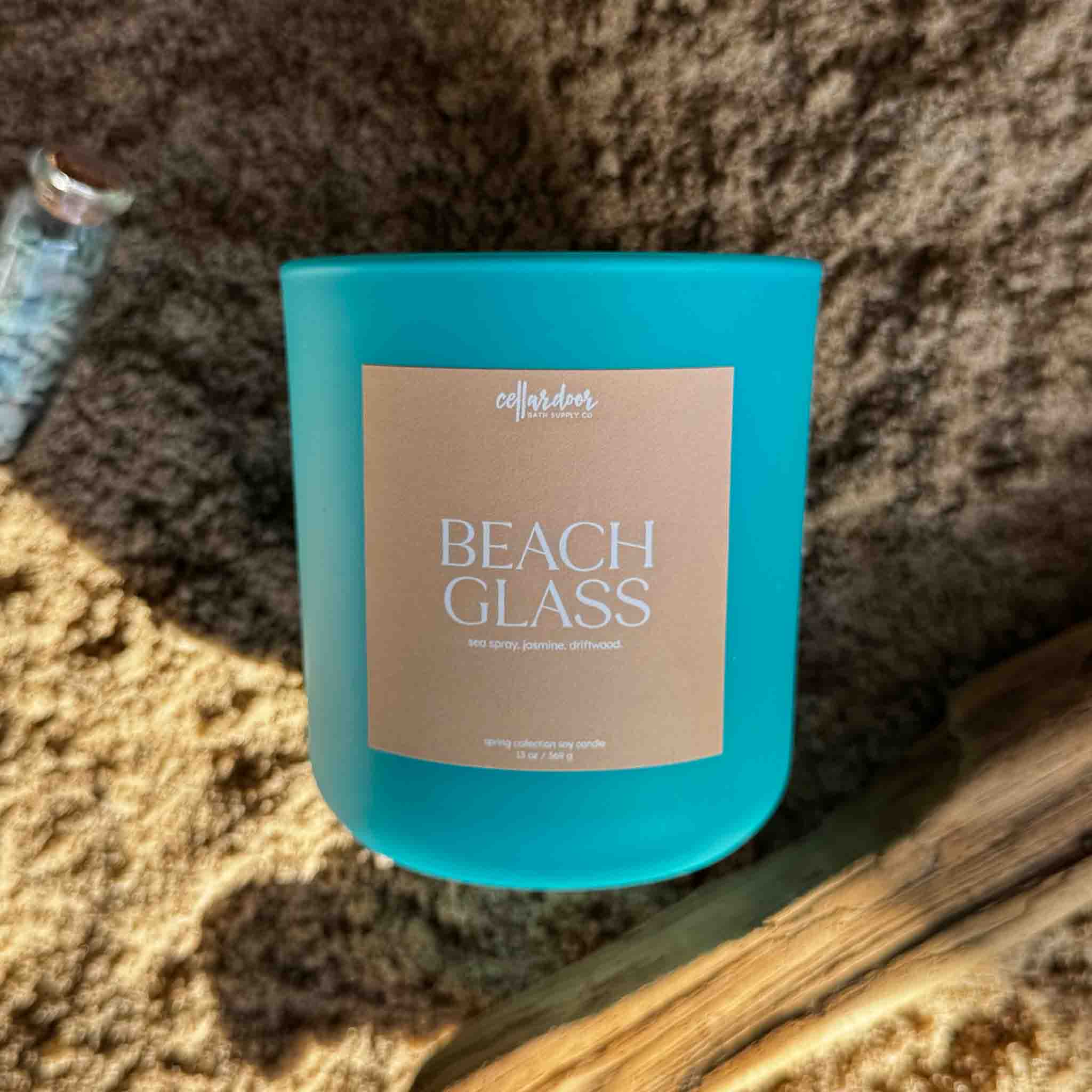 Blue candle labeled 'Beach Glass' on a sandy background