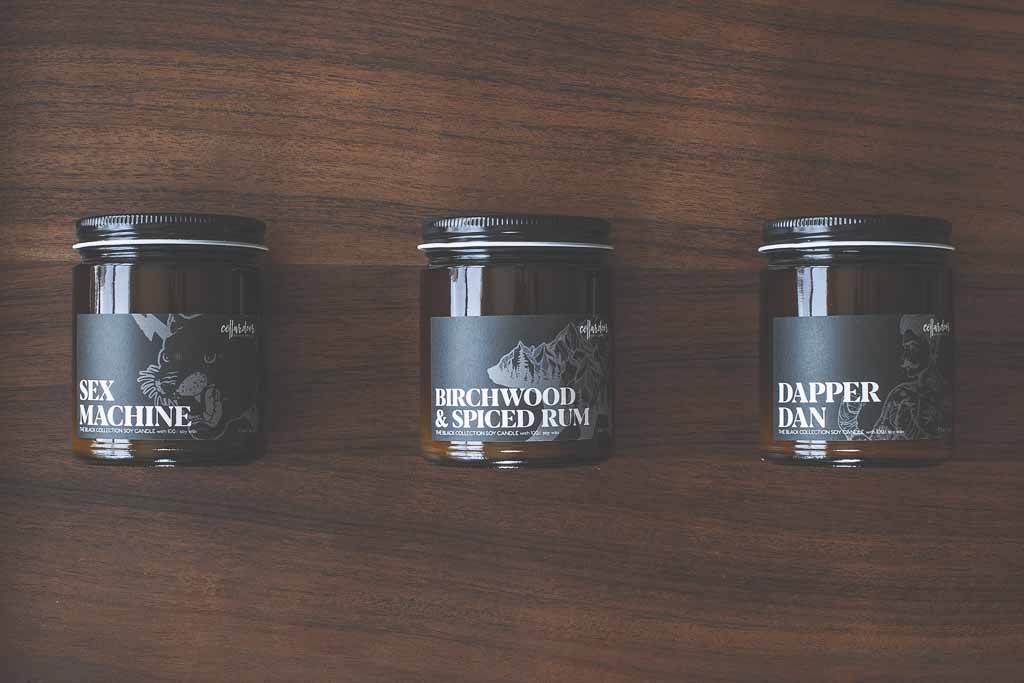 An assortment of candles in amber jars with black lids rest on a brown wood background.