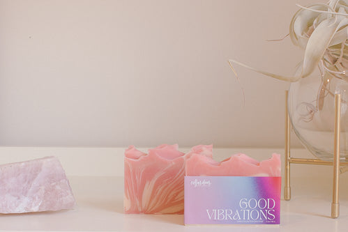 Two bars of a pink and white soap named Good Vibrations sit on a shelf.