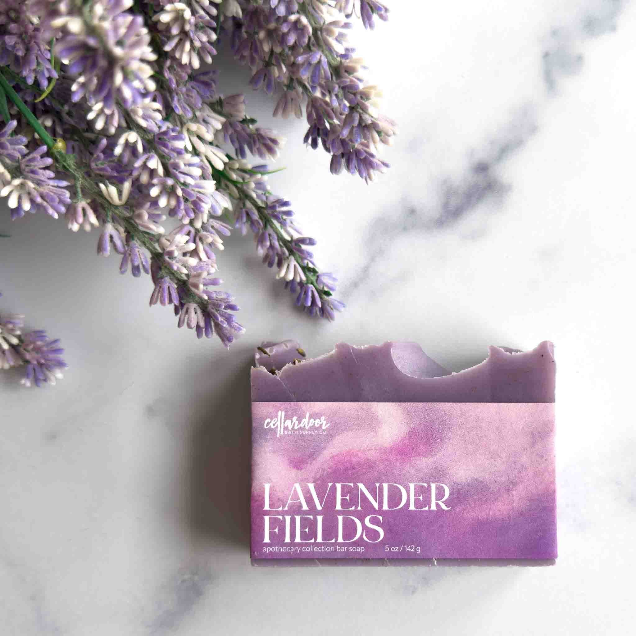 A bar of lavender soap labeled 'collaborative' and 'LAVENDER FIELDS' sits on a white marble surface next to dried lavender sprigs.