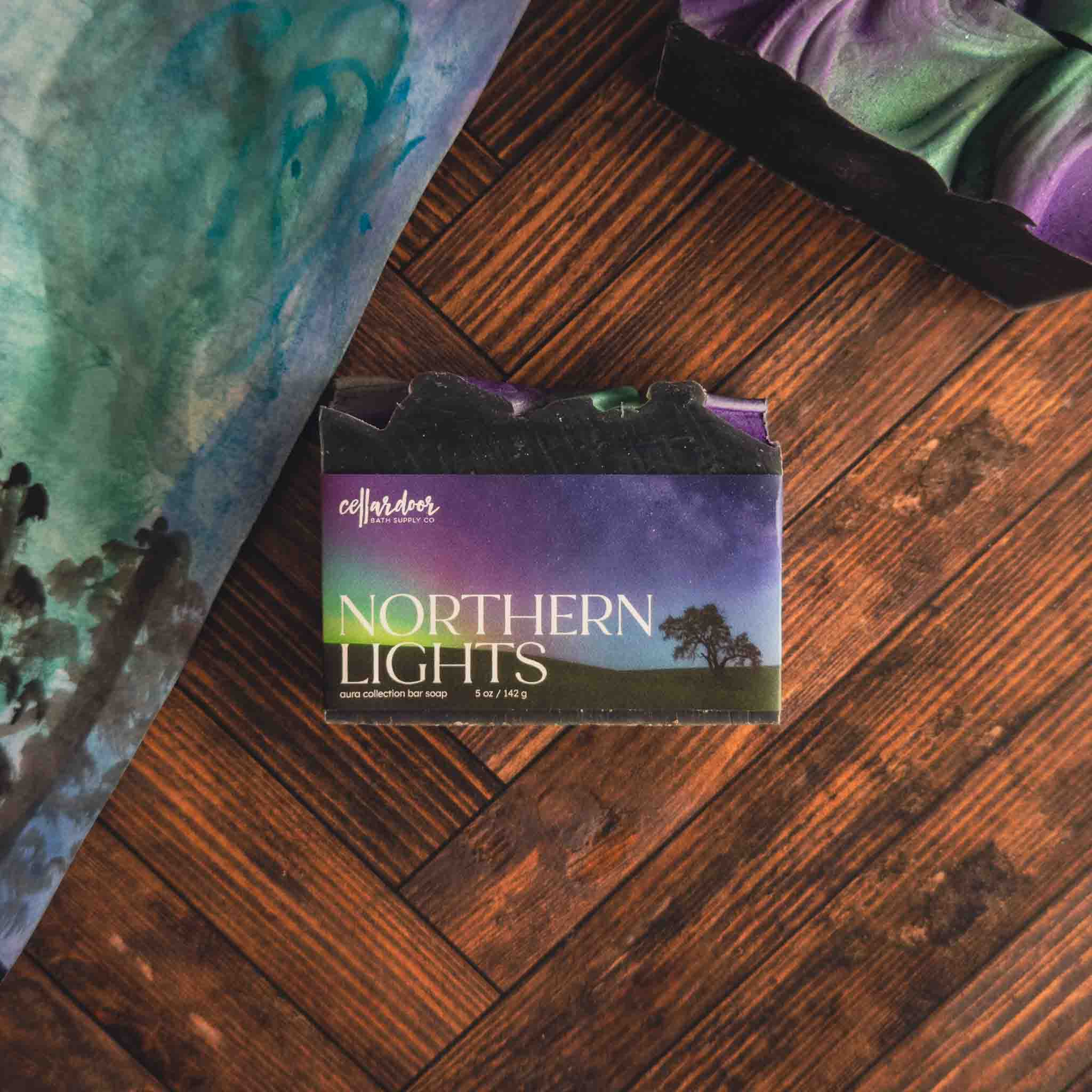 Northern Lights soap packaging on a wooden surface with tie-dye fabric in the background